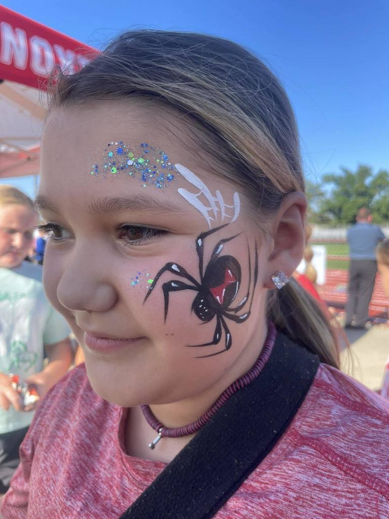 a girl wearing a red t shirt, with a black widow spider painted on the left side of her face