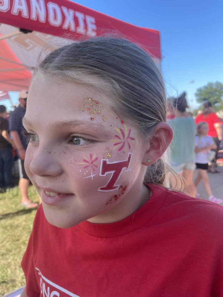a girl wearing a red t shirt, with her face painted with red and white freckles and a red Tongie T with glitter