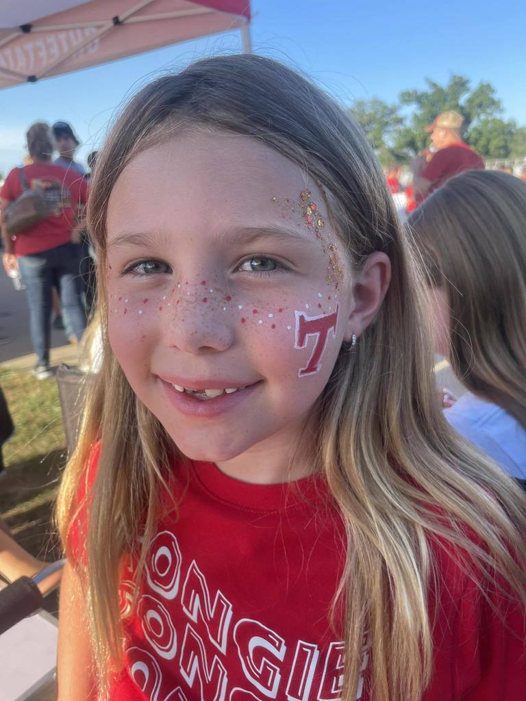 a girl wearing a red t shirt, with her face painted with red and white freckles and a red Tongie T with glitter