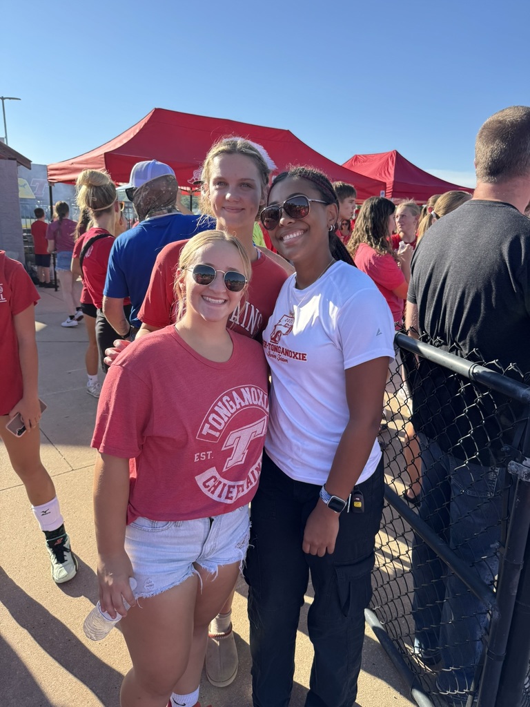 three high school girls standing together, two wear sunglasses, a chain link fence is to their left