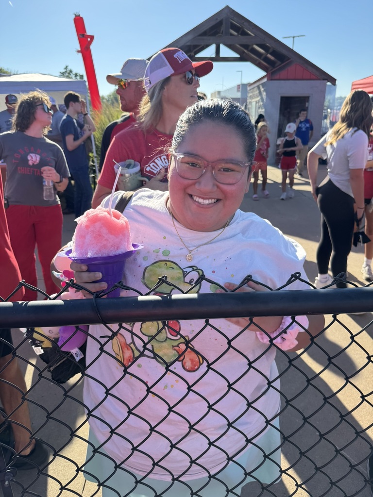 girl wearing white t shirt and teal skirt, holding a giant snocone, leaning up against a chain link fence