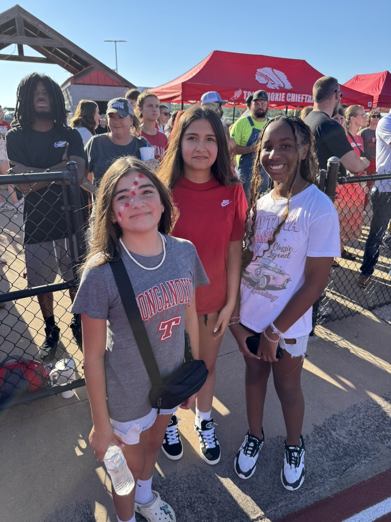 three students stand together in front of a black chain link fence