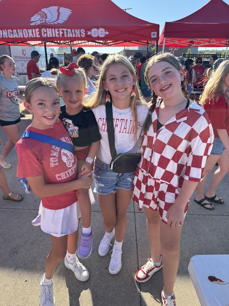 four girls wearing red and white spirit wear, two with their faces painted red and white, stand together in front of the red XC tent