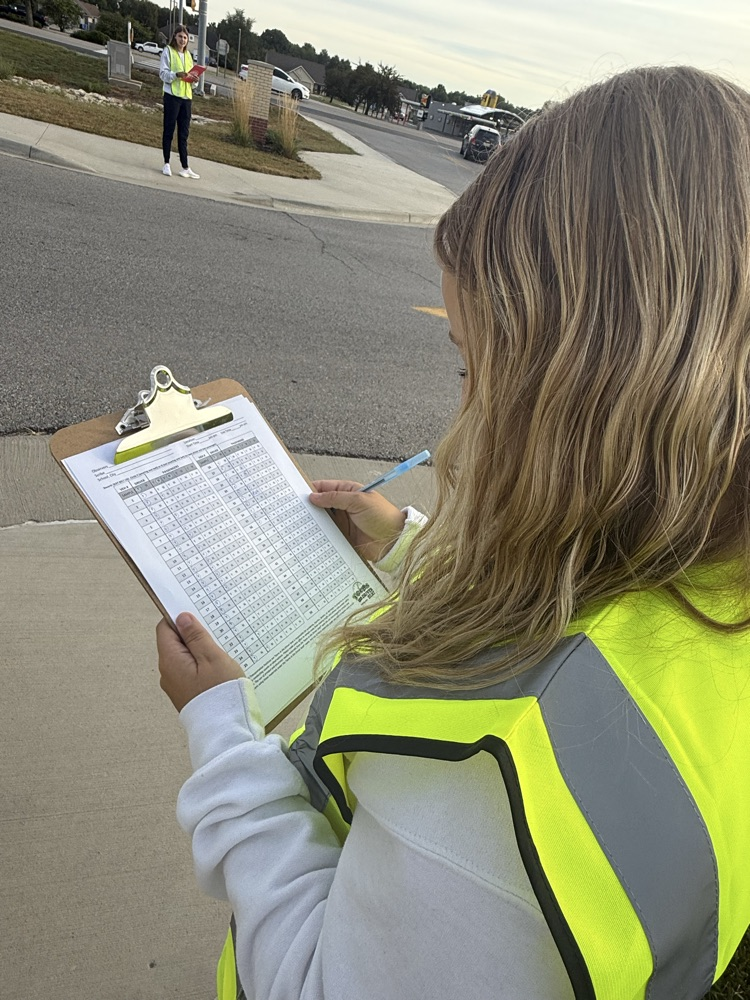 one student wearing high vis vest, holding a clipboard