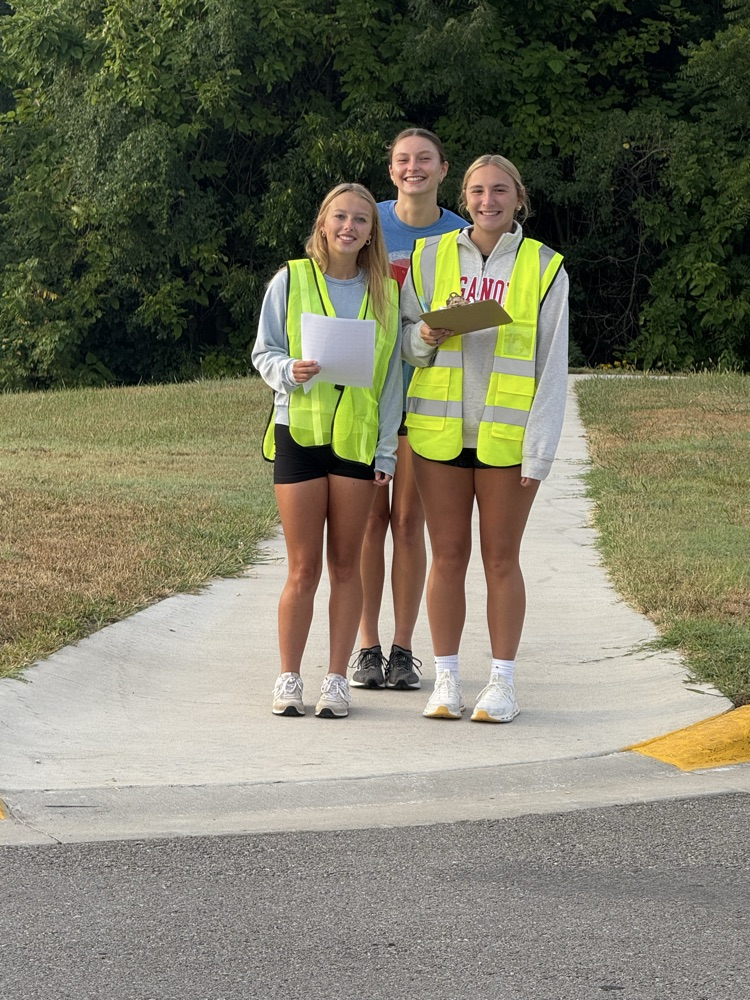 three students wearing safety vests, holding clipboards