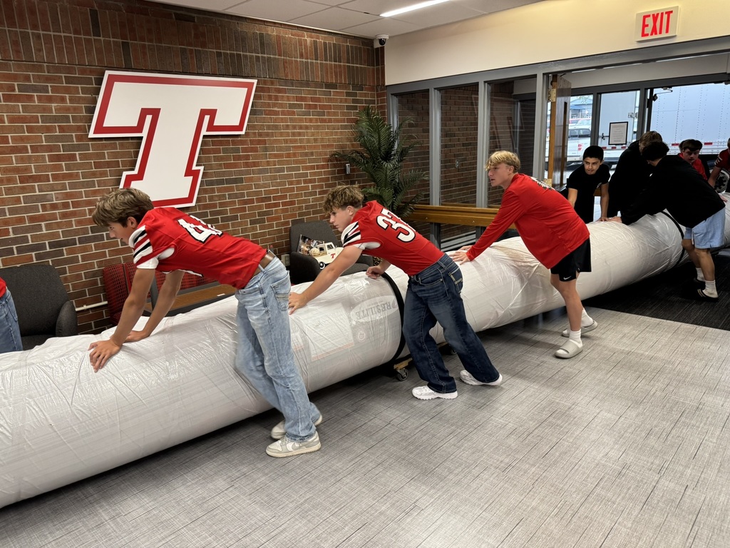 high school boys wearing red football jerseys move wrestling mats into the district administrative center