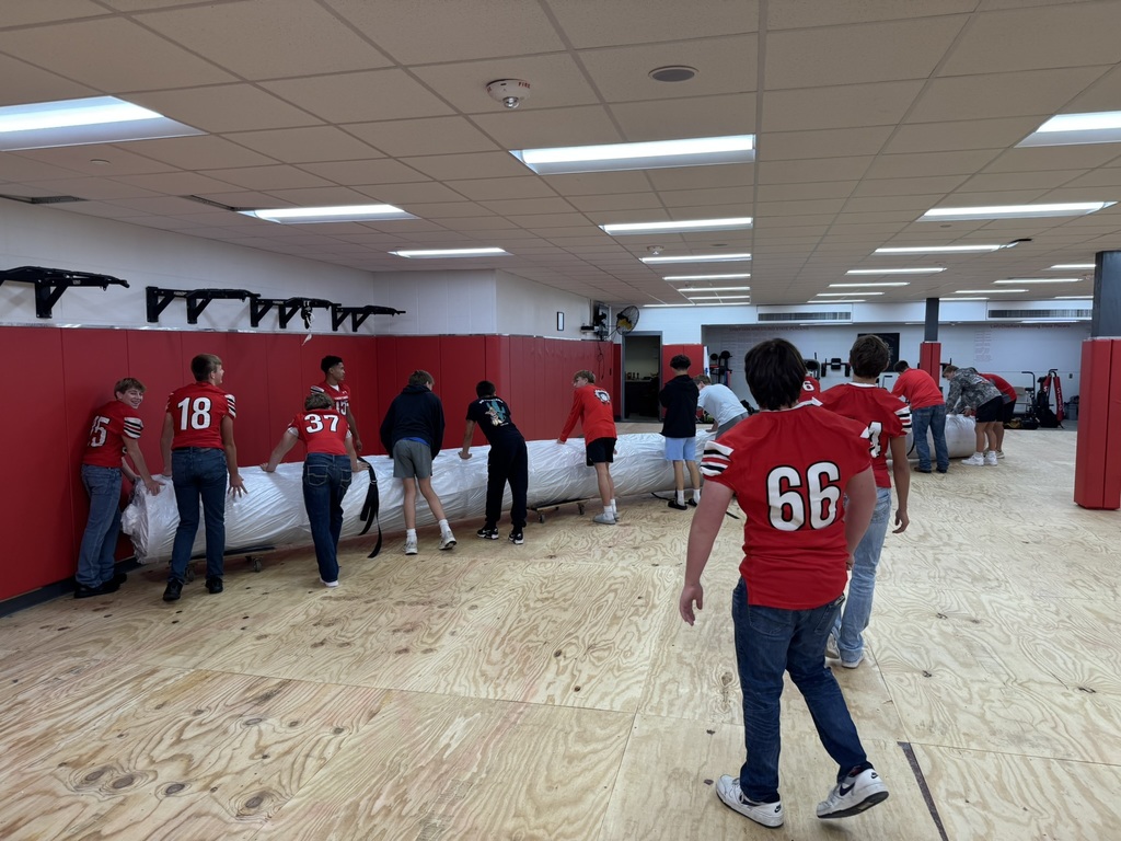 high school boys wearing red football jerseys move wrestling mats into the district administrative center