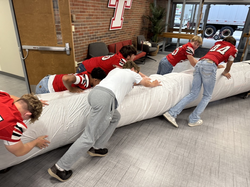 high school boys wearing red football jerseys move wrestling mats into the district administrative center
