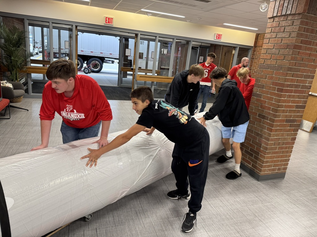 high school boys wearing red football jerseys move wrestling mats into the district administrative center
