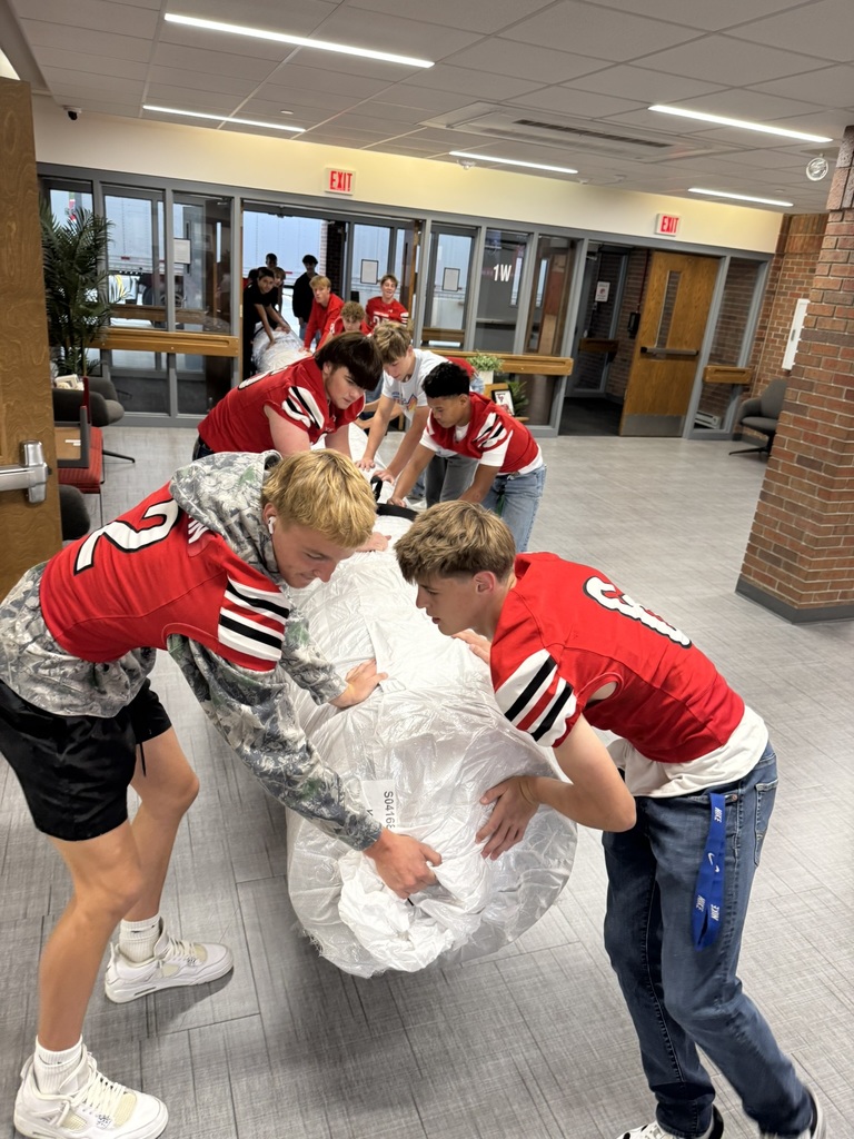 high school boys wearing red football jerseys move wrestling mats into the district administrative center