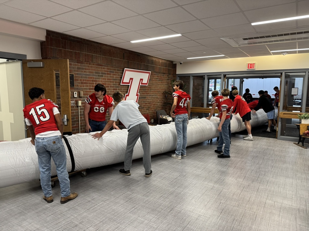 high school boys wearing red football jerseys move wrestling mats into the district administrative center
