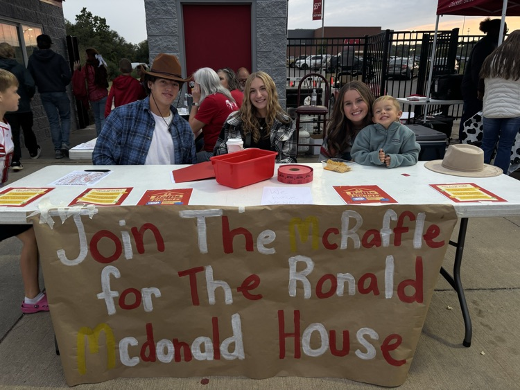 kaylin and maggie sit at a white folding table with a brown, red and white banner on the front for the ronald mcdonald raffle
