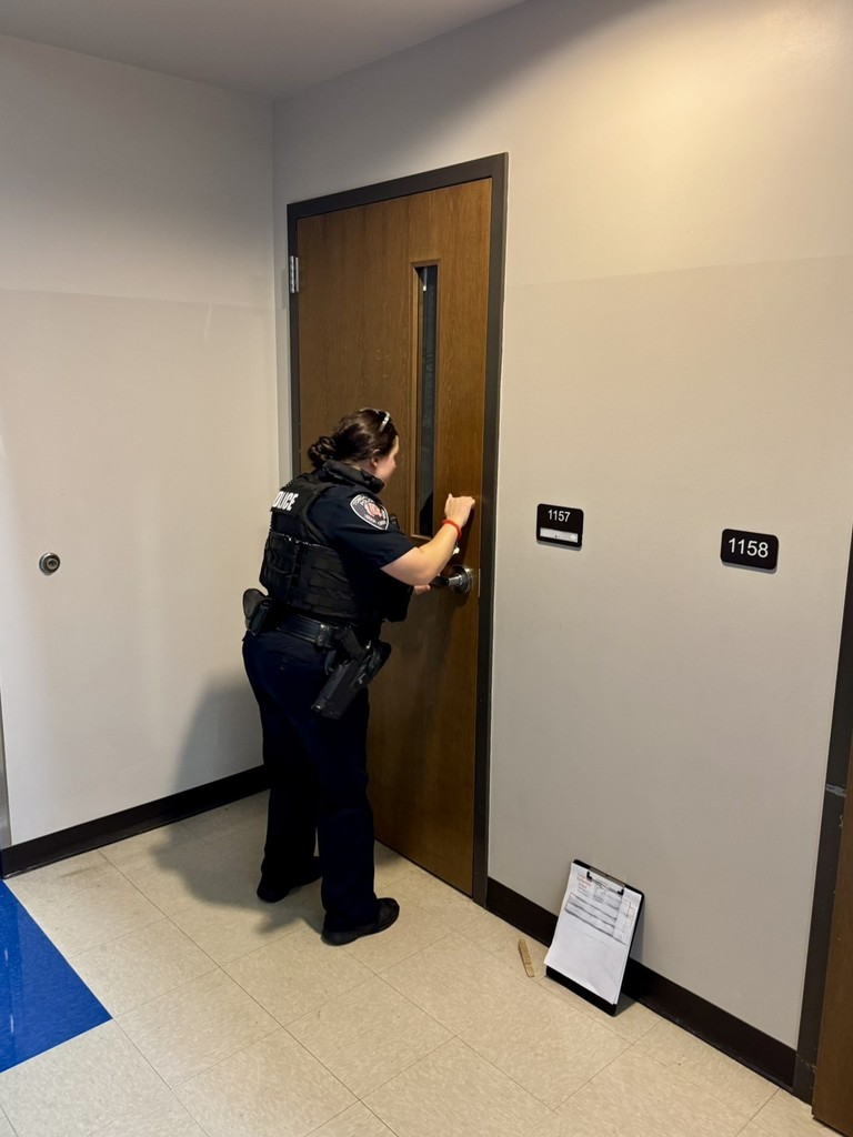Officer Kopp knocks on the brown wooden door as part of the Lockdown drill