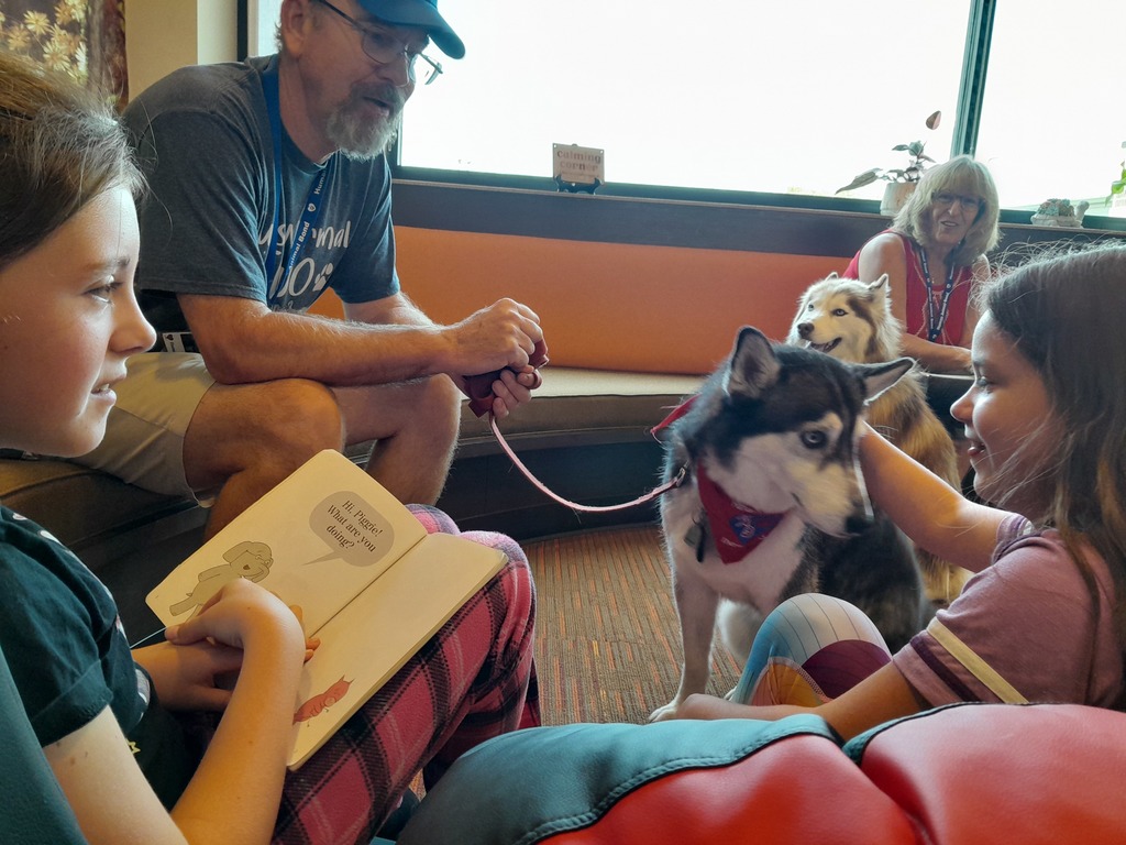 a fifth grade girl pets a husky dog wearing a red bandanna