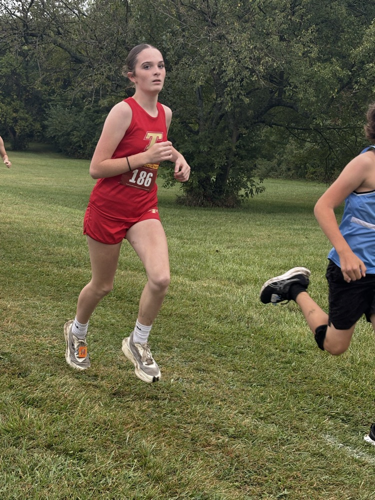 Carly wearing a red uniform running through the woods.