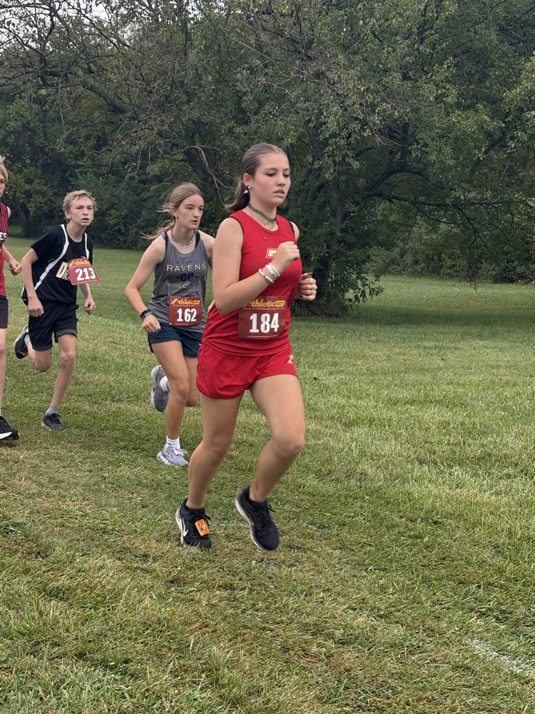 Lilly runs in a red uniform through a field.