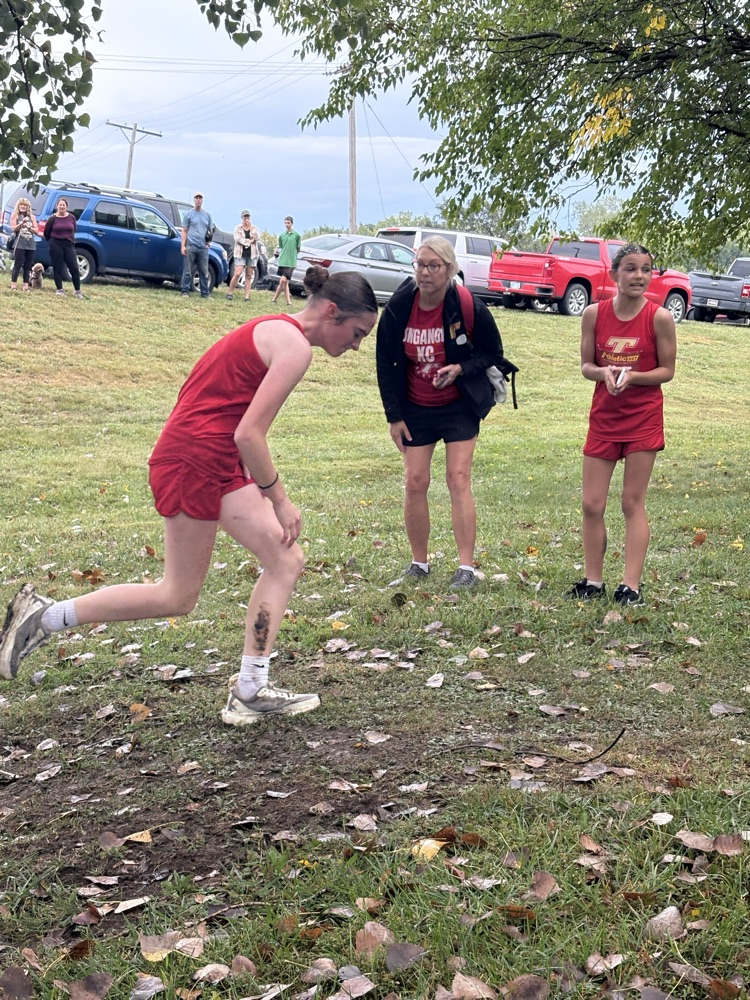 Carly hikes up a hill in a red uniform with Coach Bond cheering her on.