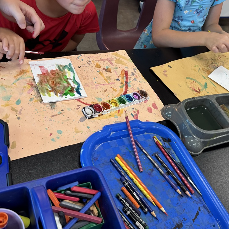two students using watercolors, one painting letters and the other trying controlled splatter painting