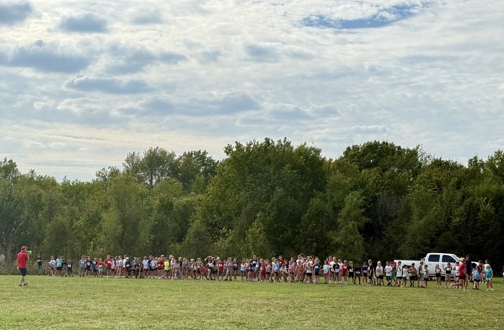 elementary school kids lined up at the race start line, a row of trees is behind them