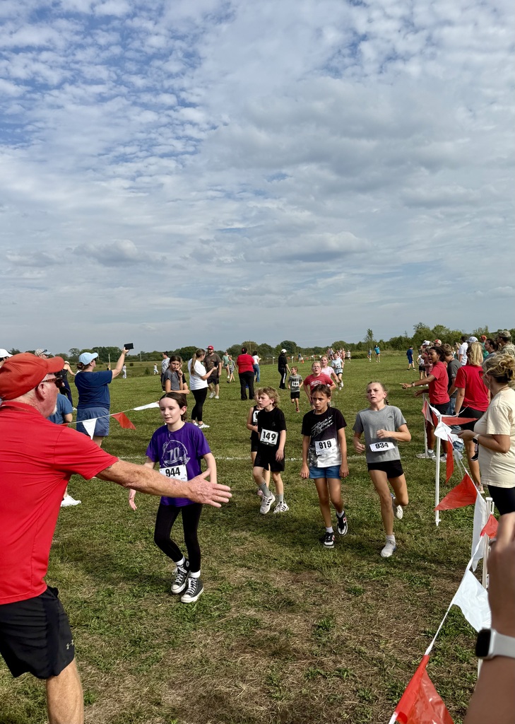 students are high fived by Coach Tollefson as they come through the finish chute, lined by red and white flags