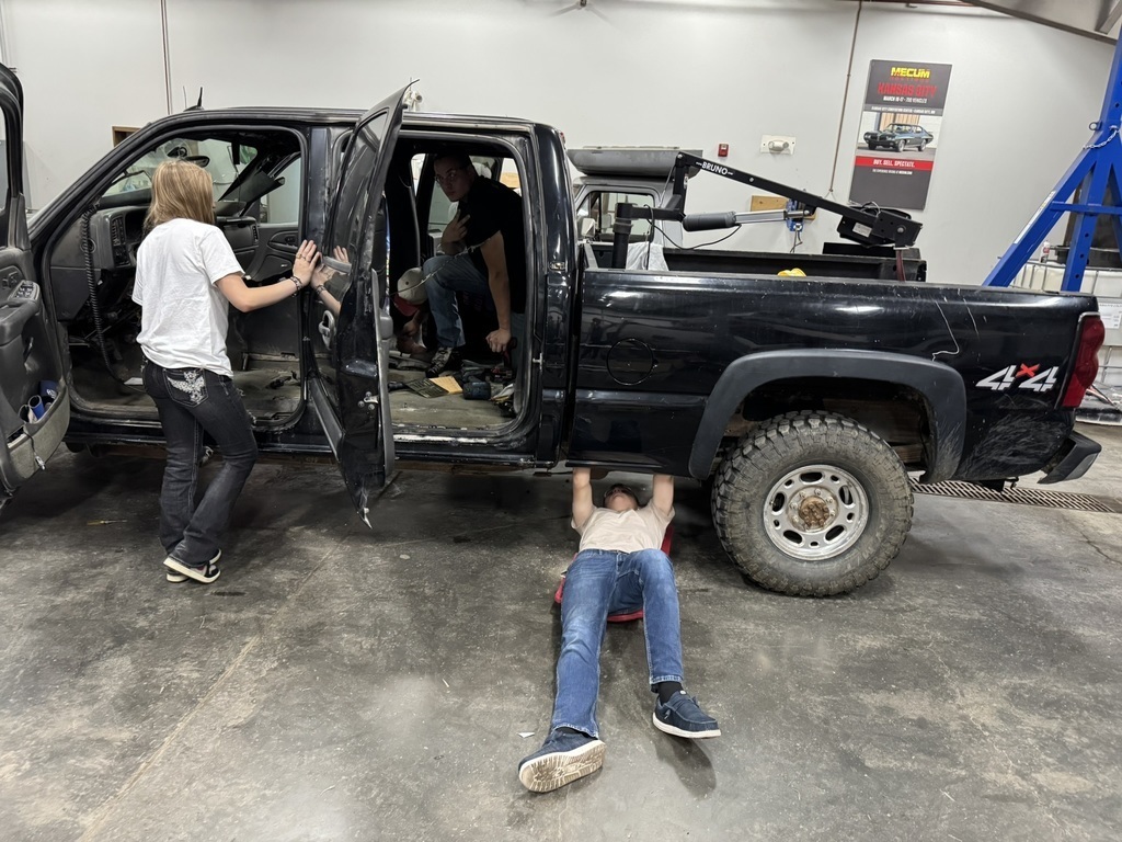 three high school students working on the inside of a black pickup truck