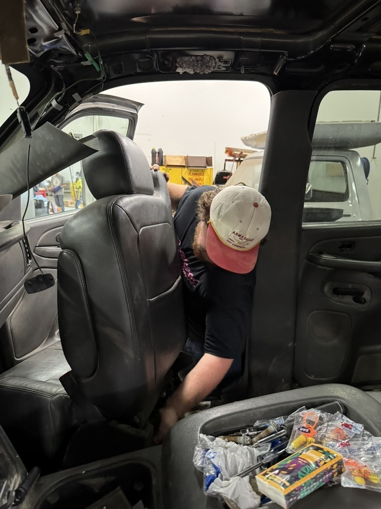a high school student wearing a black t shirt and white hat, pulling a black seat out of the front of a truck