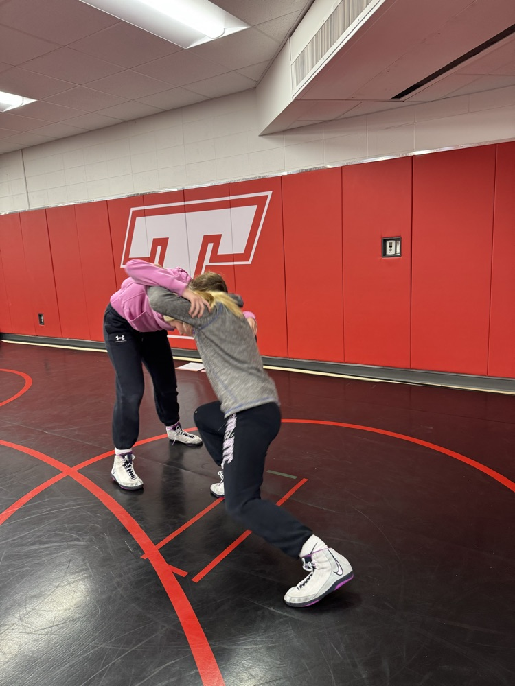 Two girls wrestling on a black wrestling mat