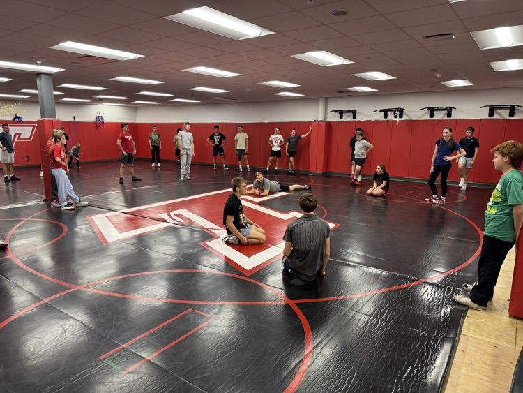 Middle school wrestlers, watching a coach demonstrated position on a black wrestling mat