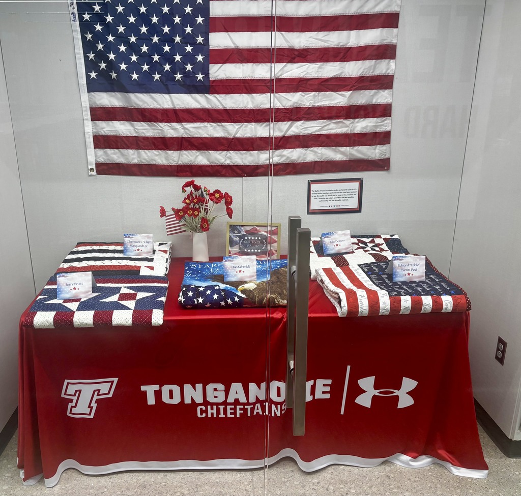 glass display case with quilts on a table and an American Flag hanging on the wall