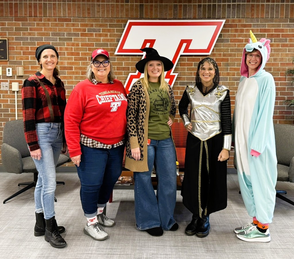 four female employees dressed up for halloween, standing in front of a brick wall with a white Tongie T on it