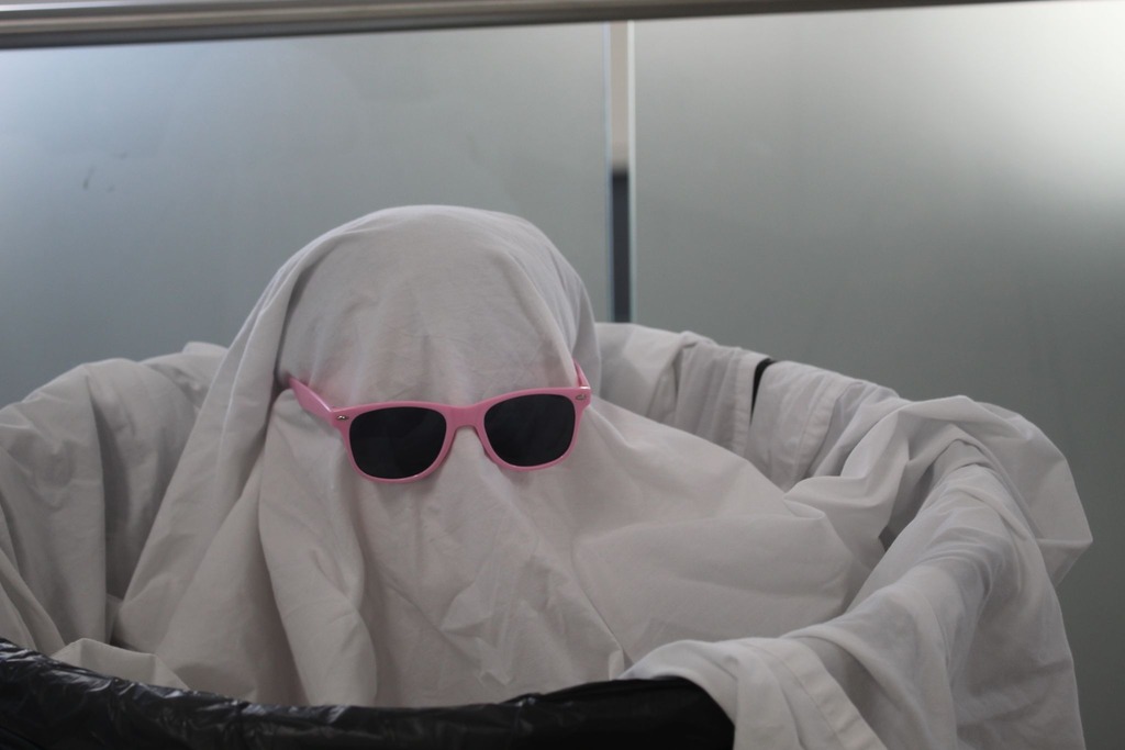 student wearing a sheet like a ghost, sitting in a trash can