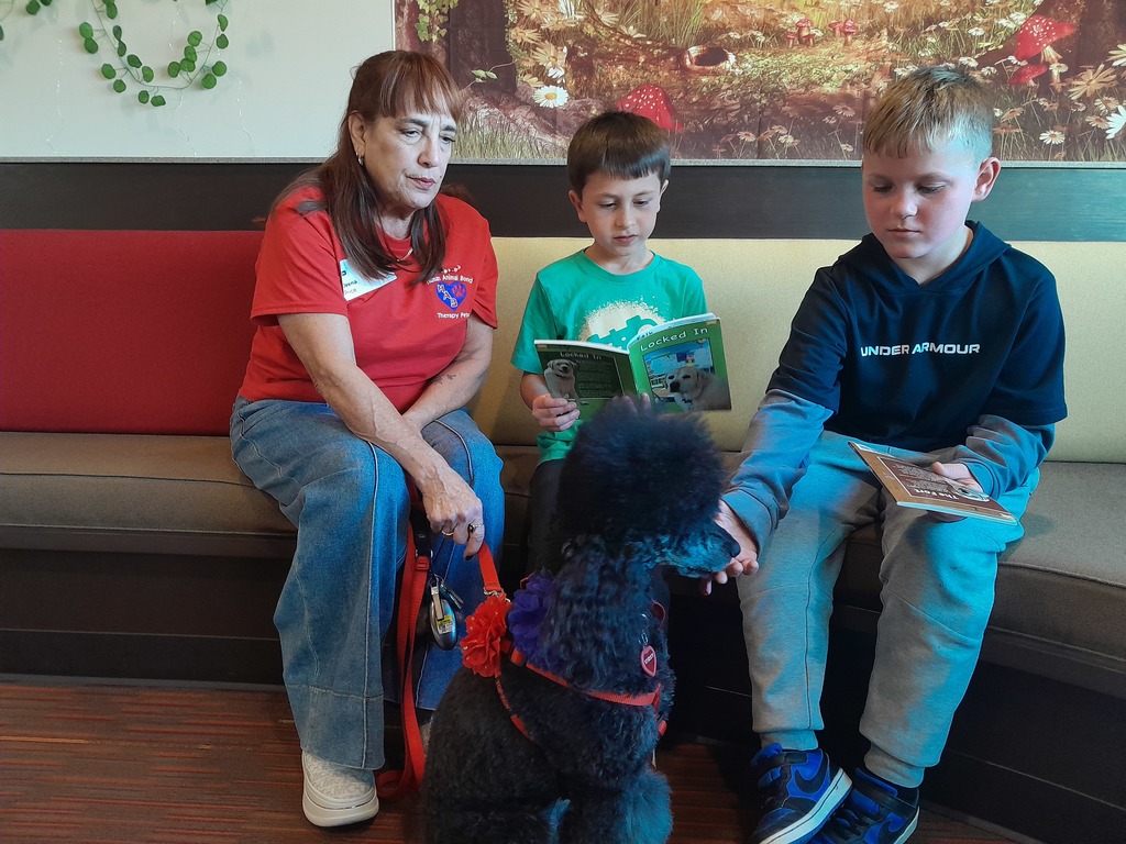 third graders sitting with a black dog wearing a red leash