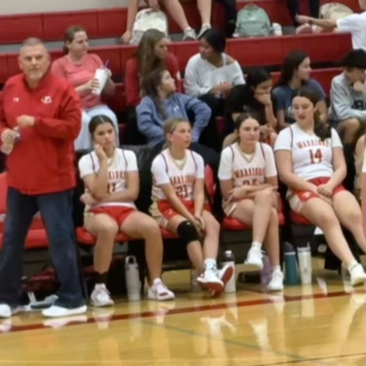 coach walking by bench filled with 4 girls .