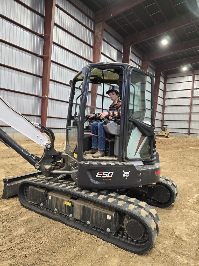 a boy in jeans and a plaid shirt operators a skidsteer