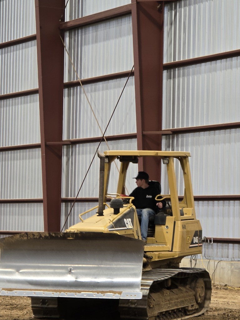 a boy in a black hoodie and jean operates a backhoe