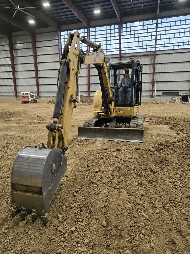 boy in a gray hoodie and jeans sitting in the cab of a bulldozer