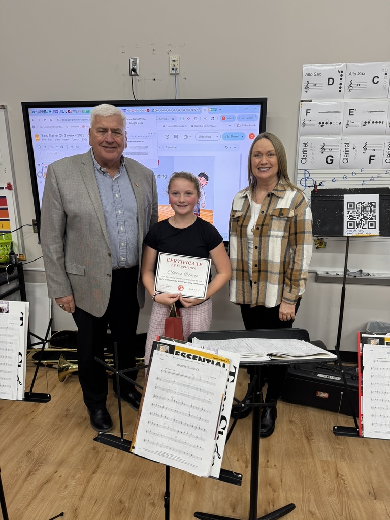 Claire standing with Mr. Feldkamp and Mrs. Phillips in a classroom with a digital smartboard on the wall behind them