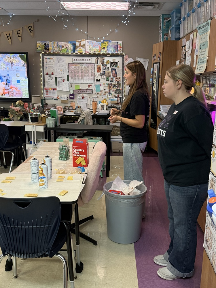 two high schoolers stand at the front of a classroom speaking to fifth grade students