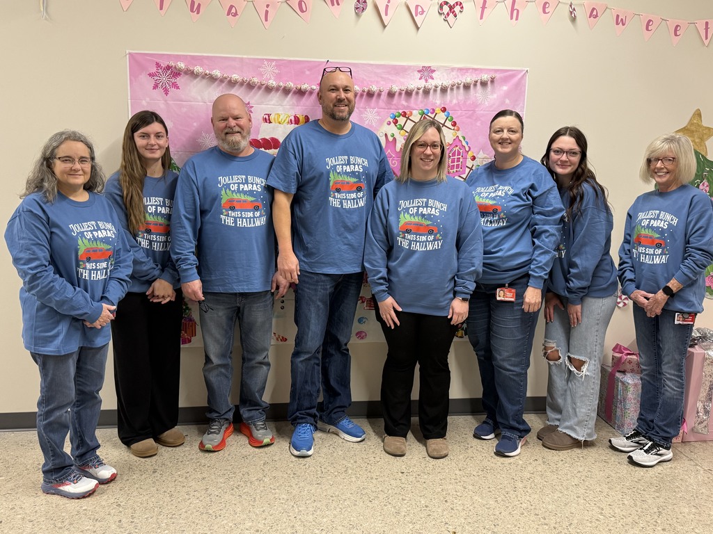 eight adults wearing matching long sleeved t shirts with a red van with a pine tree on top, with the words "jolliest bunch of paras this side of the hallway"