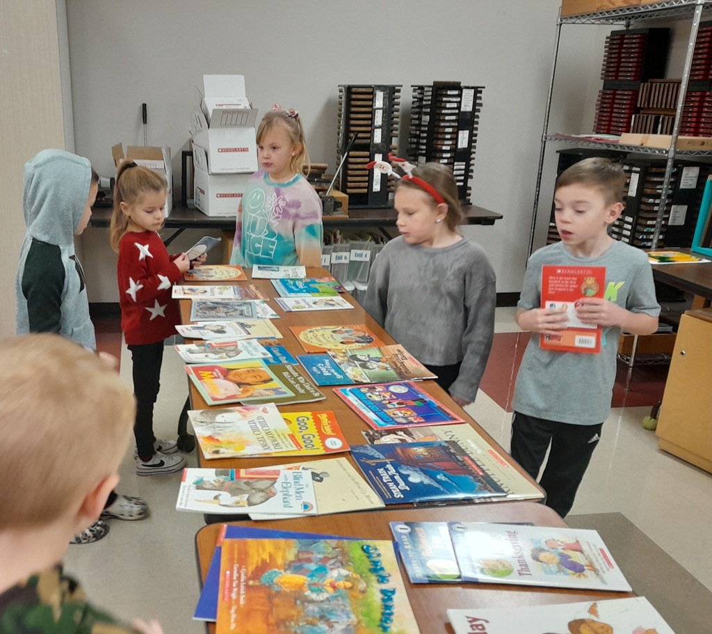 Elementary students picking out books laying on a brown wooden table