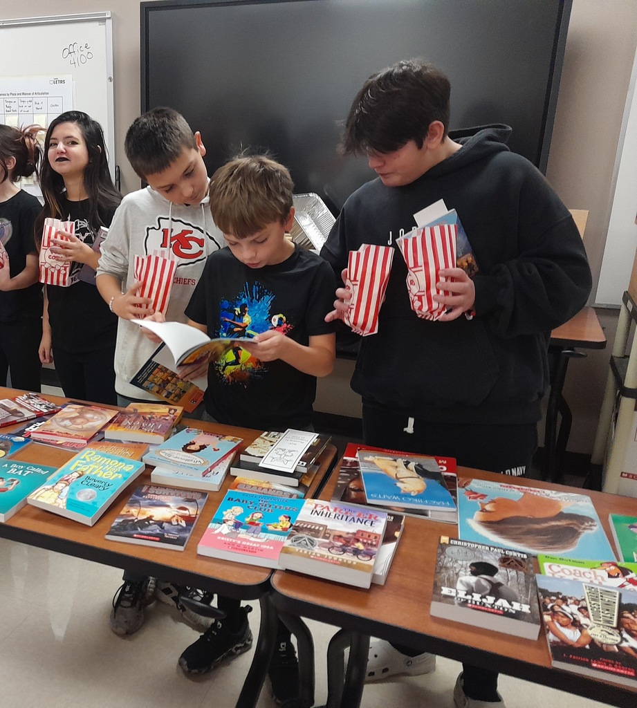 Elementary students picking out books laying on a brown wooden table