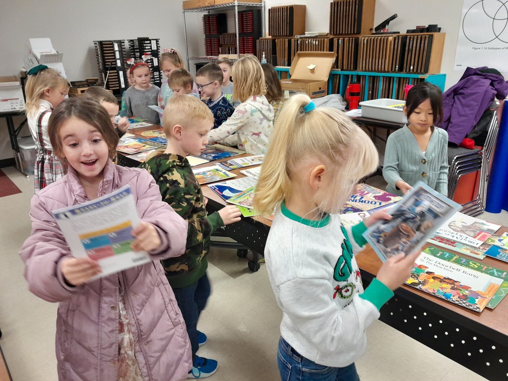 Elementary students picking out books laying on a brown wooden table