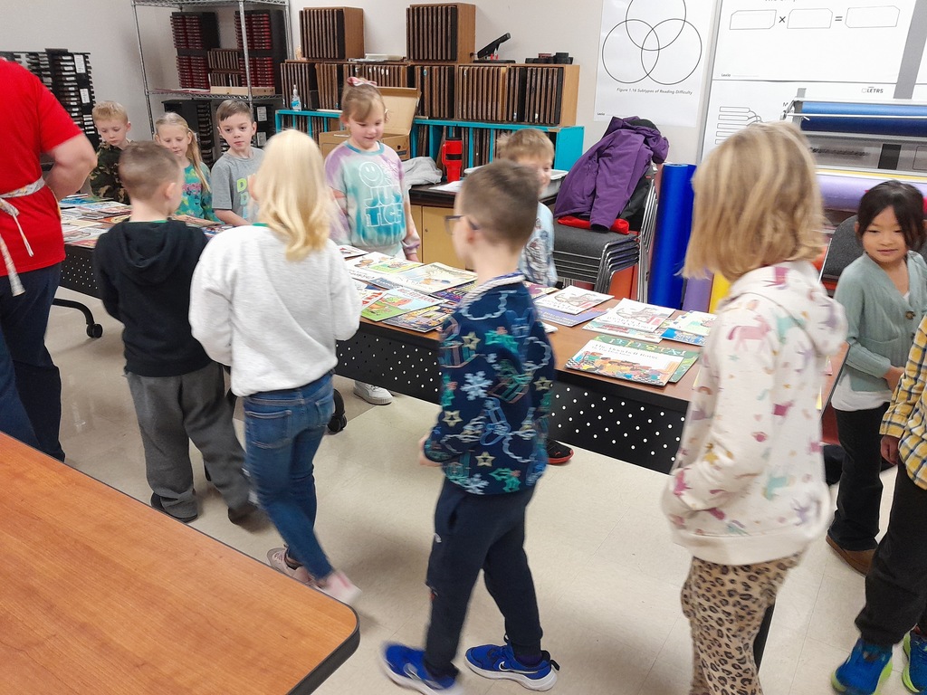 Elementary students picking out books laying on a brown wooden table