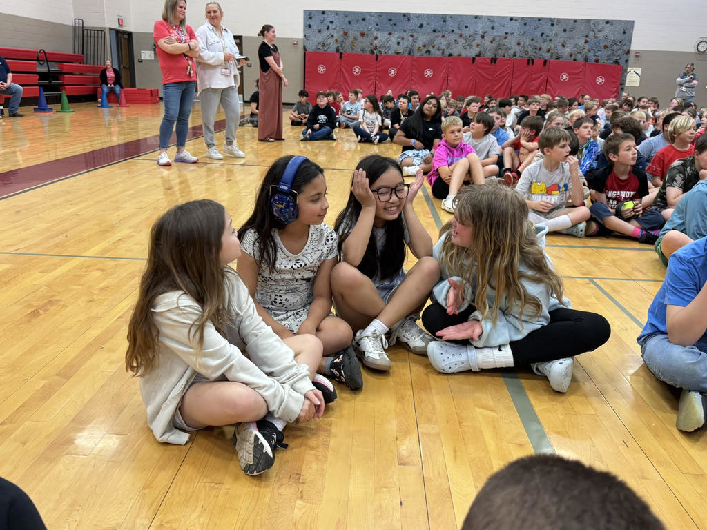 four third grade girls sit on a wooden gymnasium floor