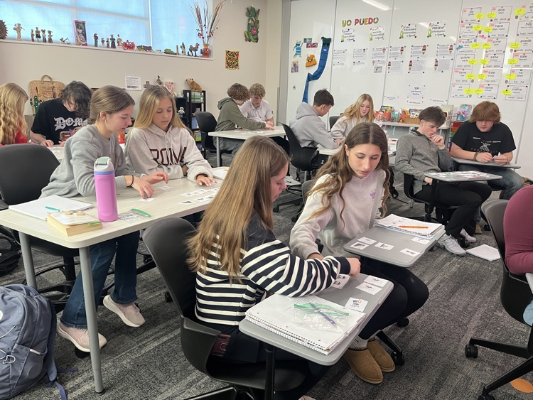 Pairs of students are sitting at tables and desks, working with sequencing cards to create a story.
