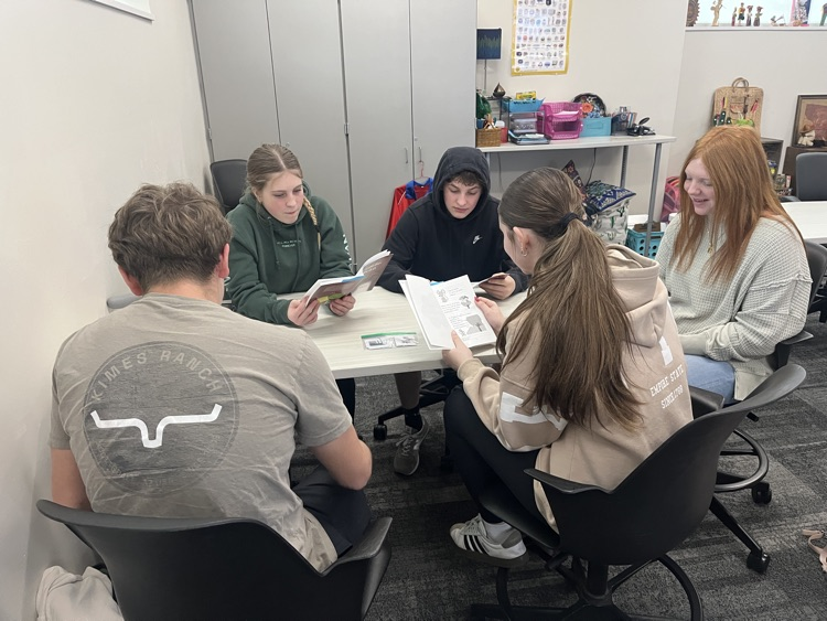 A group of students, sitting around a table, are reading a novel in Spanish.