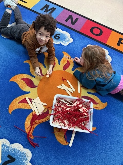 Students using wood sticks and pipe cleaners to create a leprechaun trap.