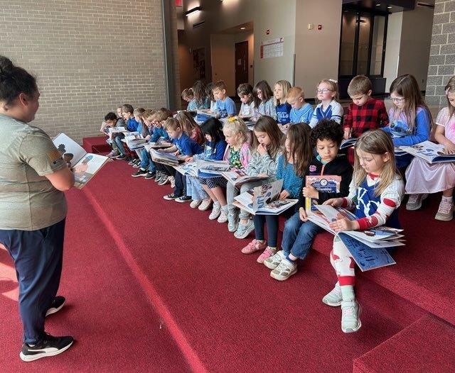Kindergarten students listening to a teacher read their new book from the Royals Reading Foundation.