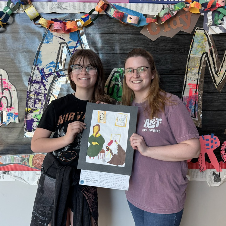 Paisley and Miss Dombeck holding Paisley’s artwork in front of a bulletin board