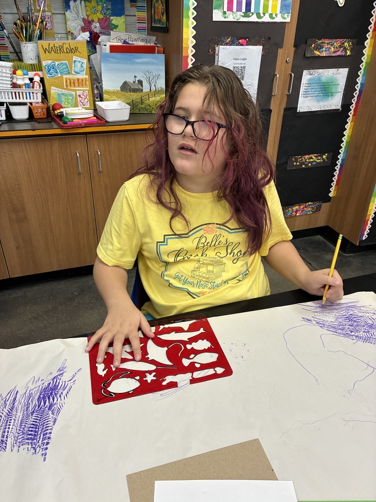 Girl in yellow shirt and glasses using a sea life stencil on big paper. 